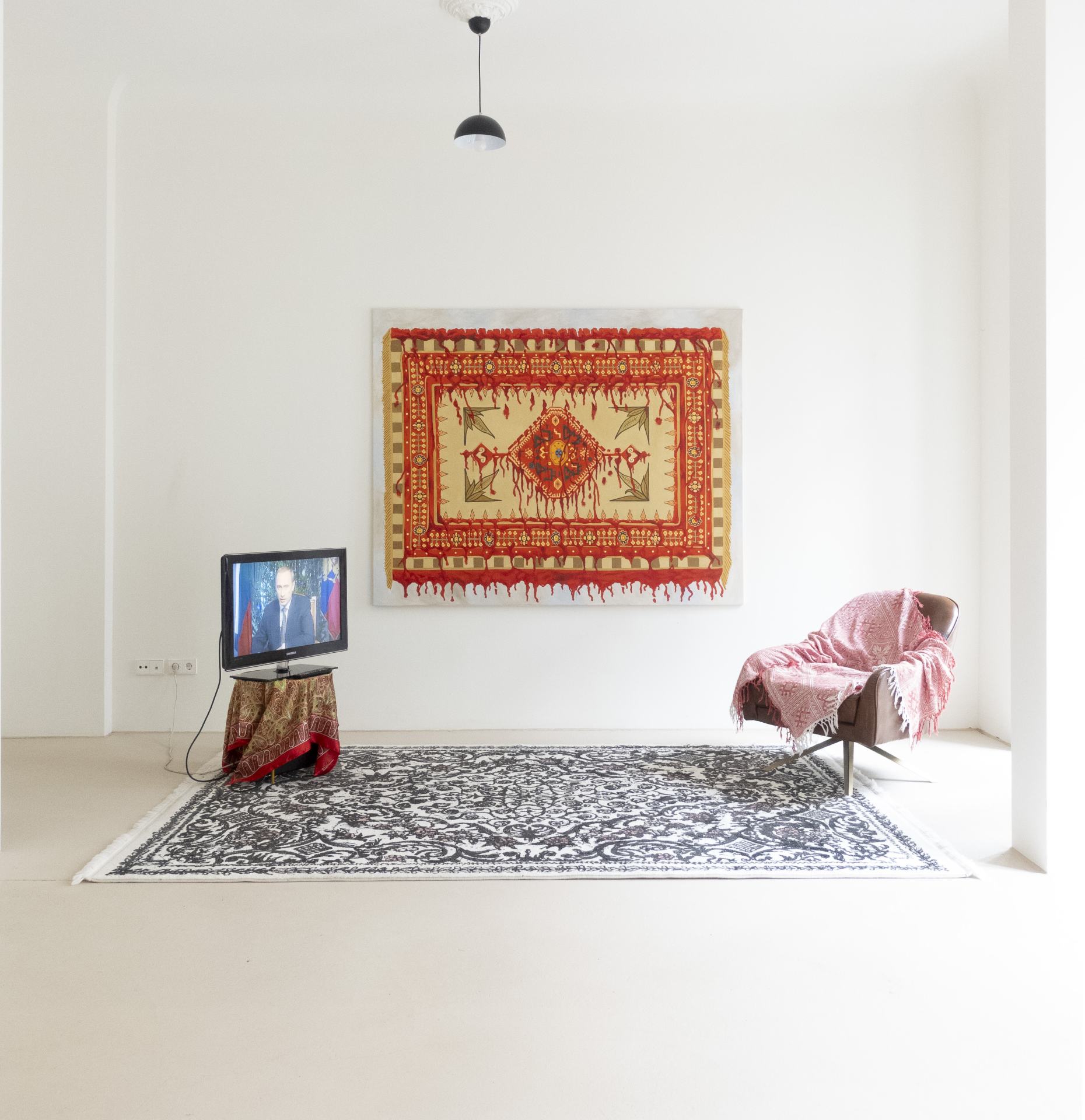 Minimalistisch eingerichteter Raum mit einem Fernseher, einem Sessel mit Decke und einem Wandteppich