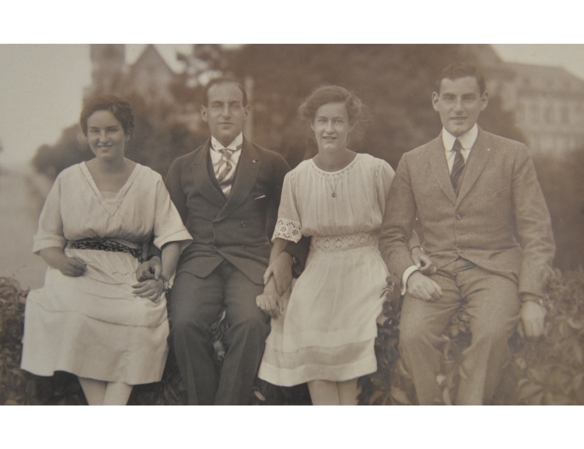 Ein schwarz-weiß Foto zeigt zwei Frauen und zwei Männer, die nebeneinander auf einer Hecke sitzen.