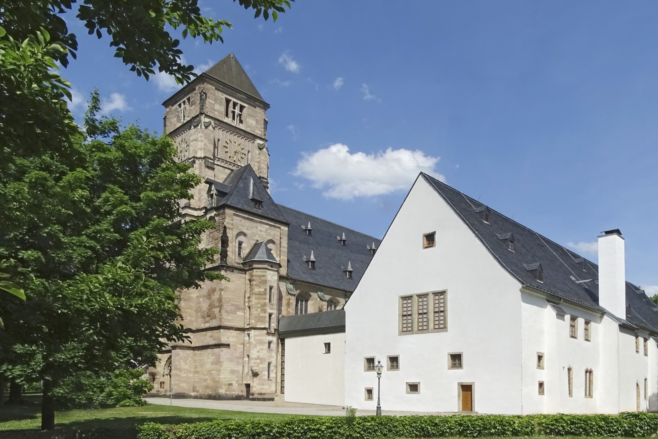 Blick auf ein weiß gestrichenes Haus, dahinter ein kirchenähnliches Gebäude