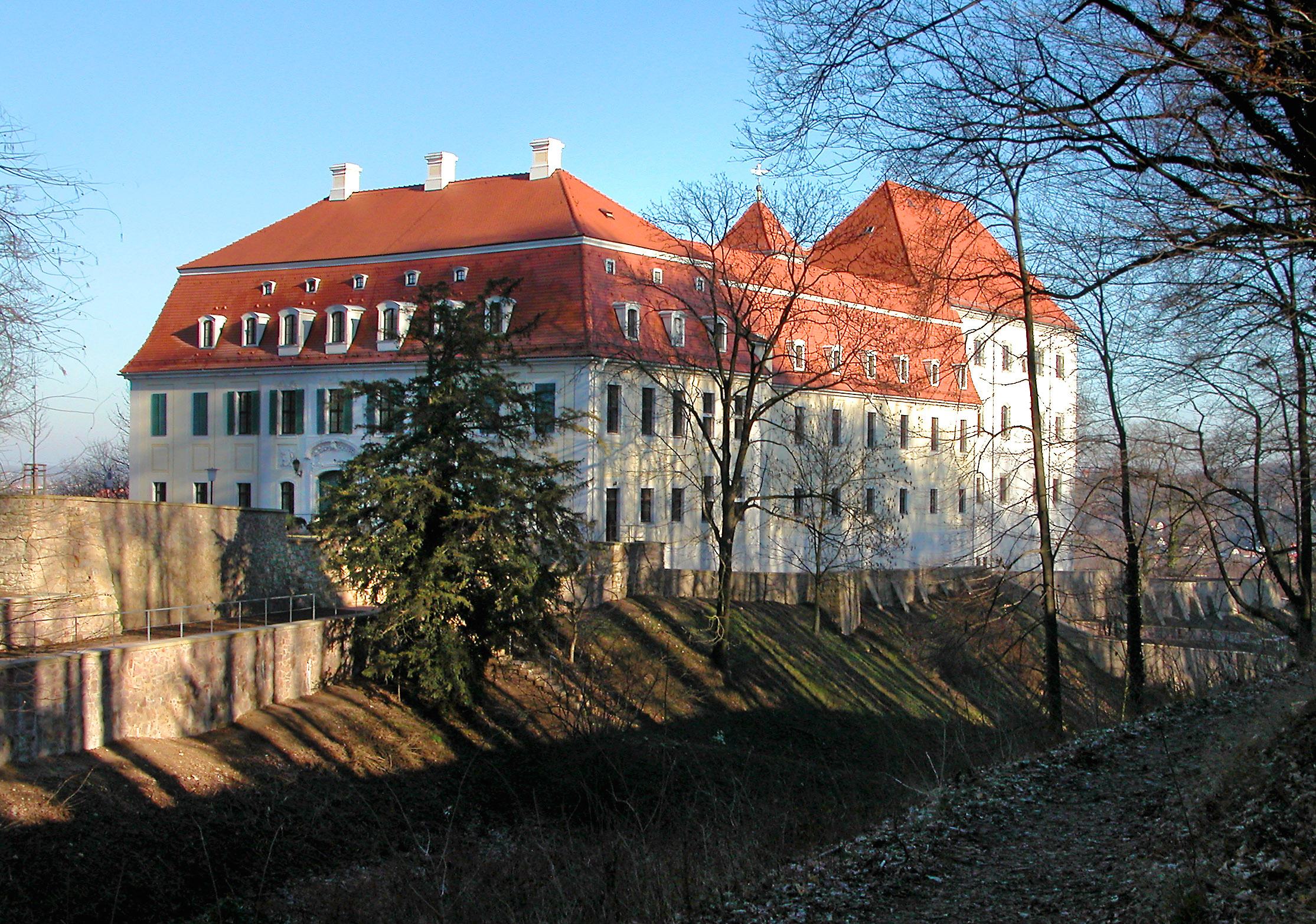 Ein hell gestrichenes Schloss mit rotem Dach hinter Bäumen