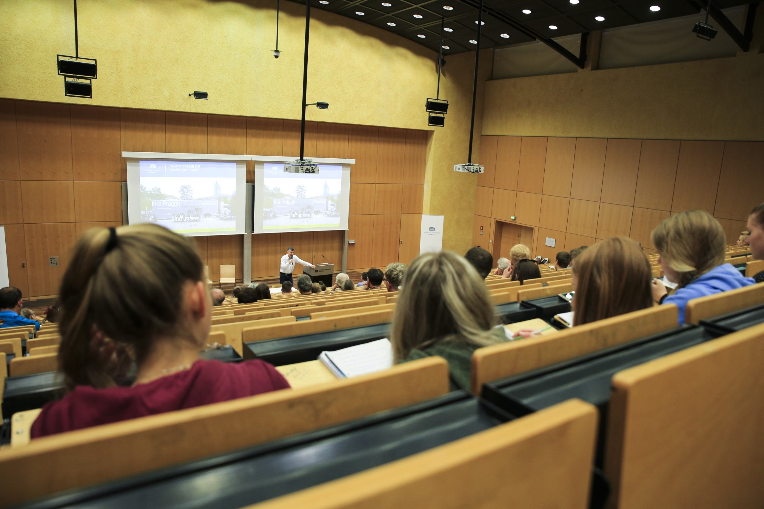 Ein Mann steht an einem Lesepult in einem Hörsaal. Davor sind Studierende zu sehen, die ihm zuhören.